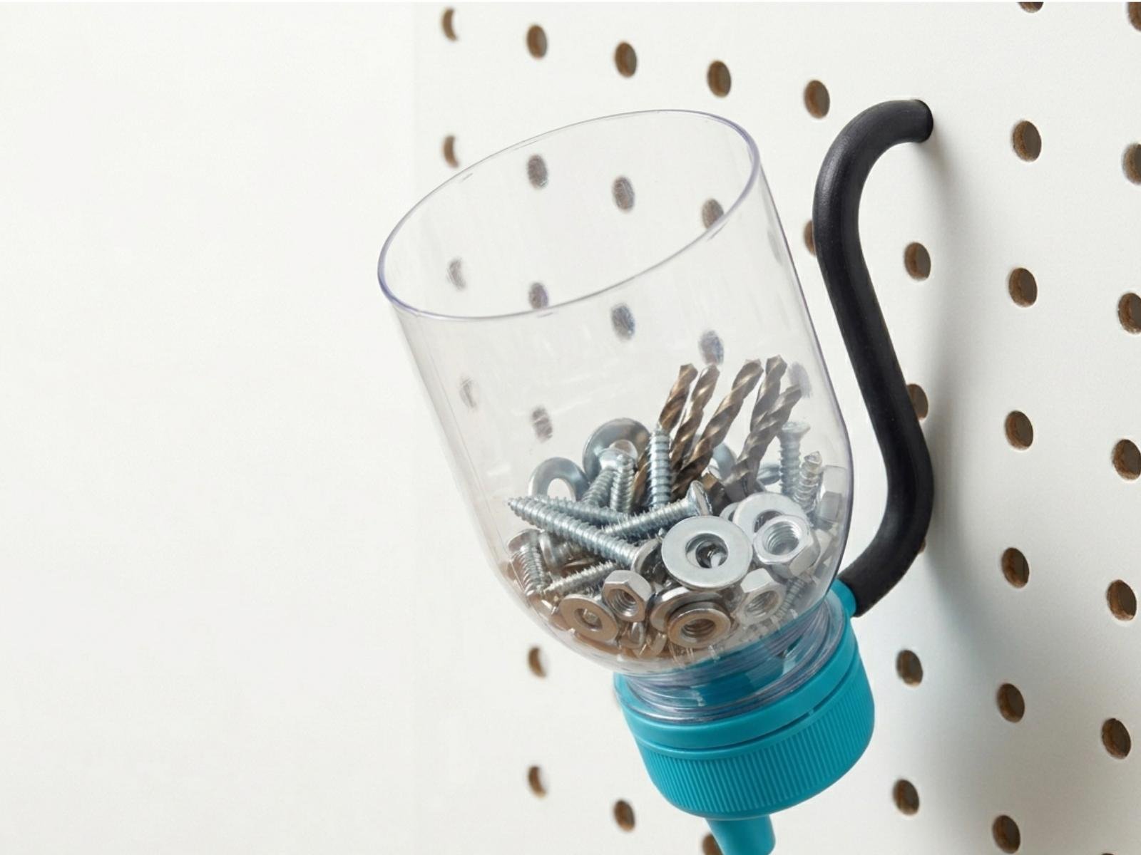 CapTool Peg cap with an angled S-hook on the back, holding a clear plastic bottle bottom hanging from a pegboard, filled with assorted screws and small hardware
