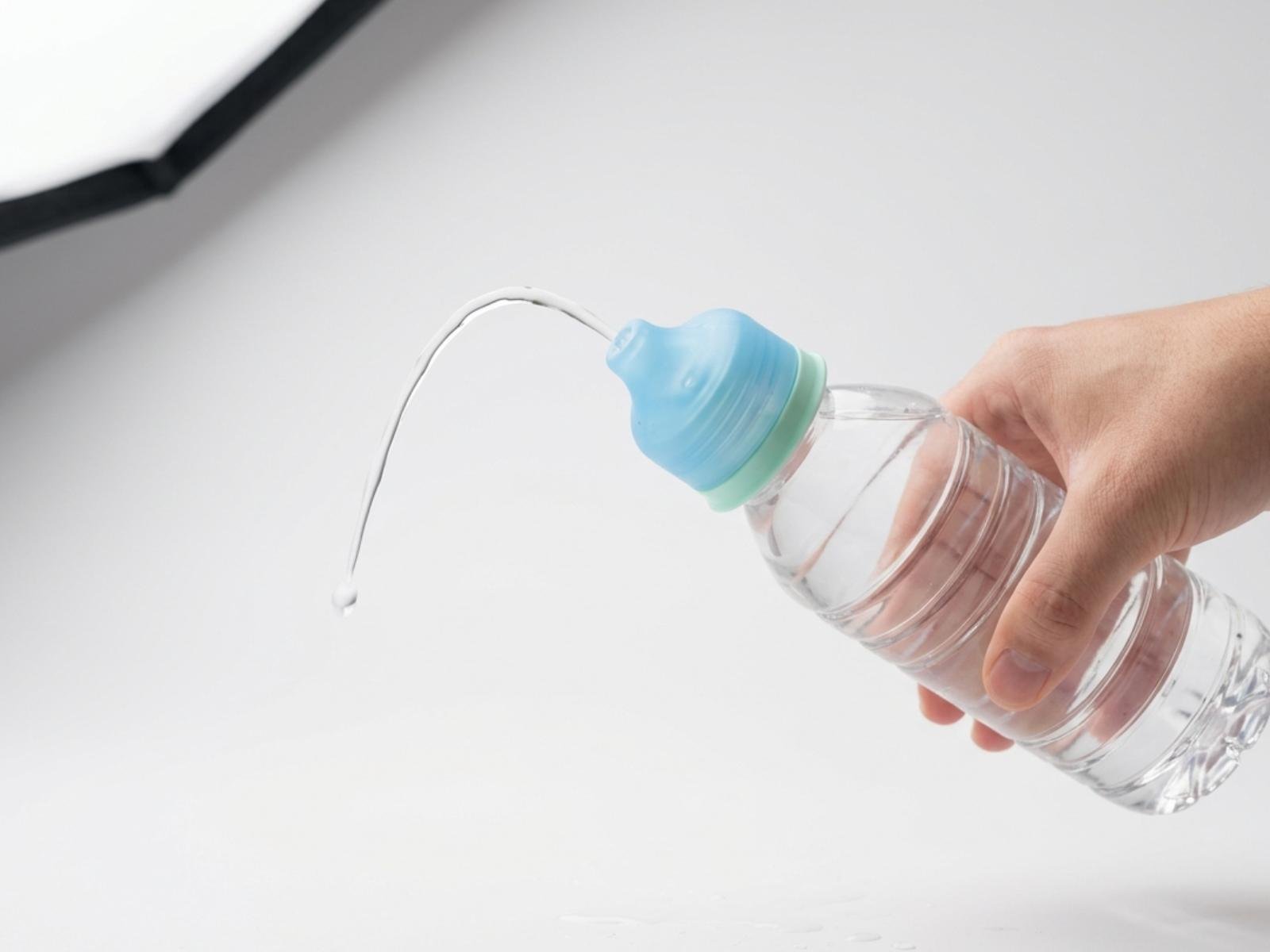 CapTool Rinse cap in translucent sky blue with mint green accent, snapped onto a clear plastic bottle, hand squeezing a thin arc of water from the nozzle